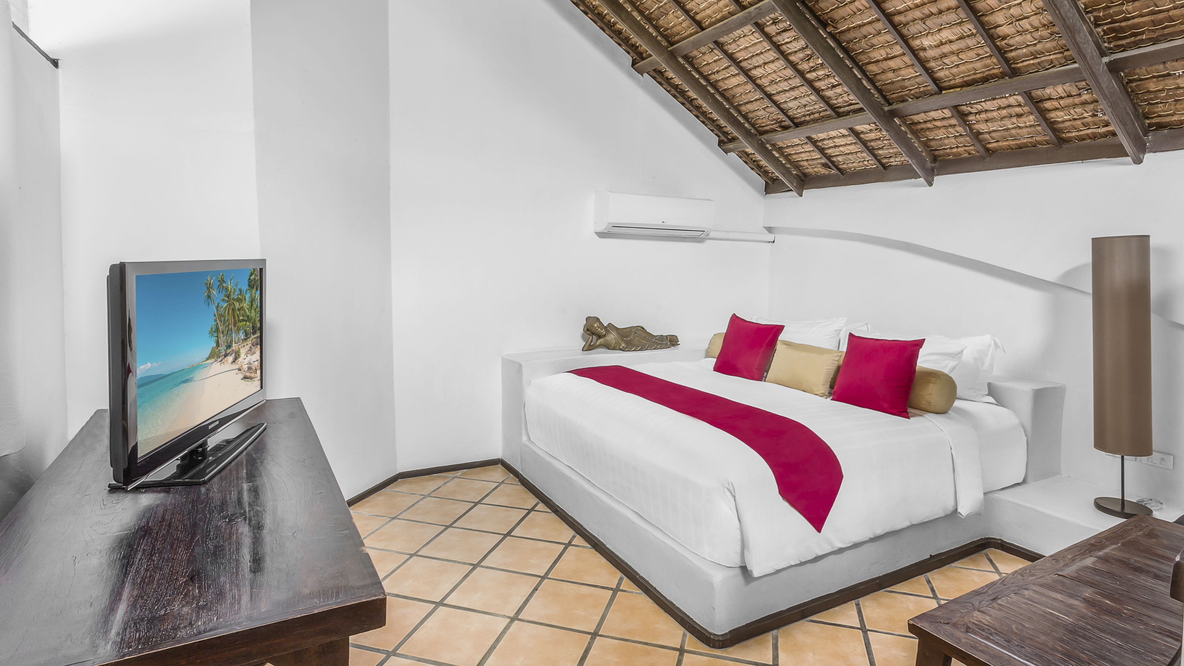Een hotelkamer met een bed, een televisie op een houten tafeltje, een groot raam en een plafondventilator.