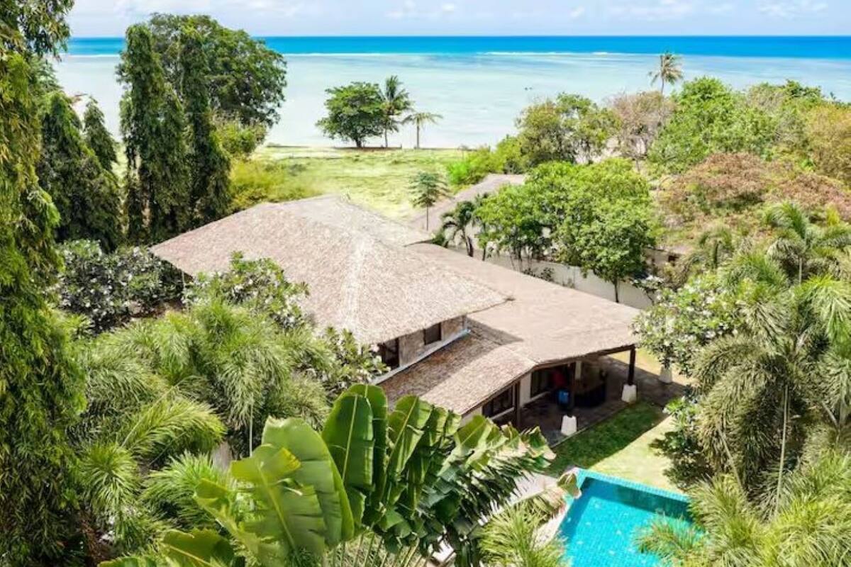 A house with a thatched roof, surrounded by lush greenery and a swimming pool.