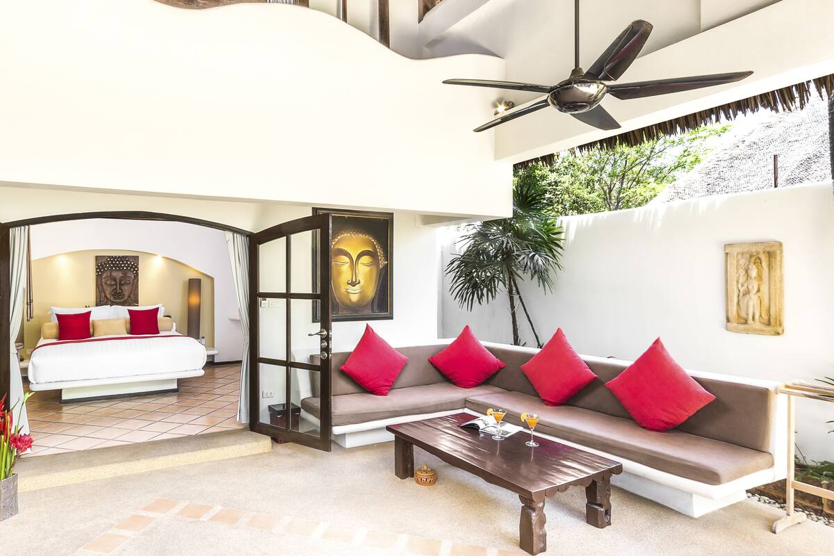 A modern hotel room with a bed, a sofa, a coffee table, and a ceiling fan.