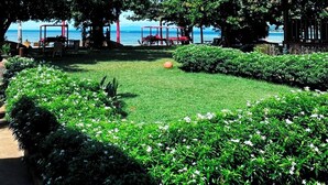 A garden area with a thatched-roof structure, lush greenery, and a view of the sea. - Beach Republic, Koh Samui (Koh Samui)