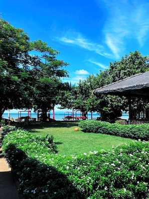 A garden area with a thatched-roof structure, lush greenery, and a view of the sea. - Beach Republic, Koh Samui (Koh Samui)