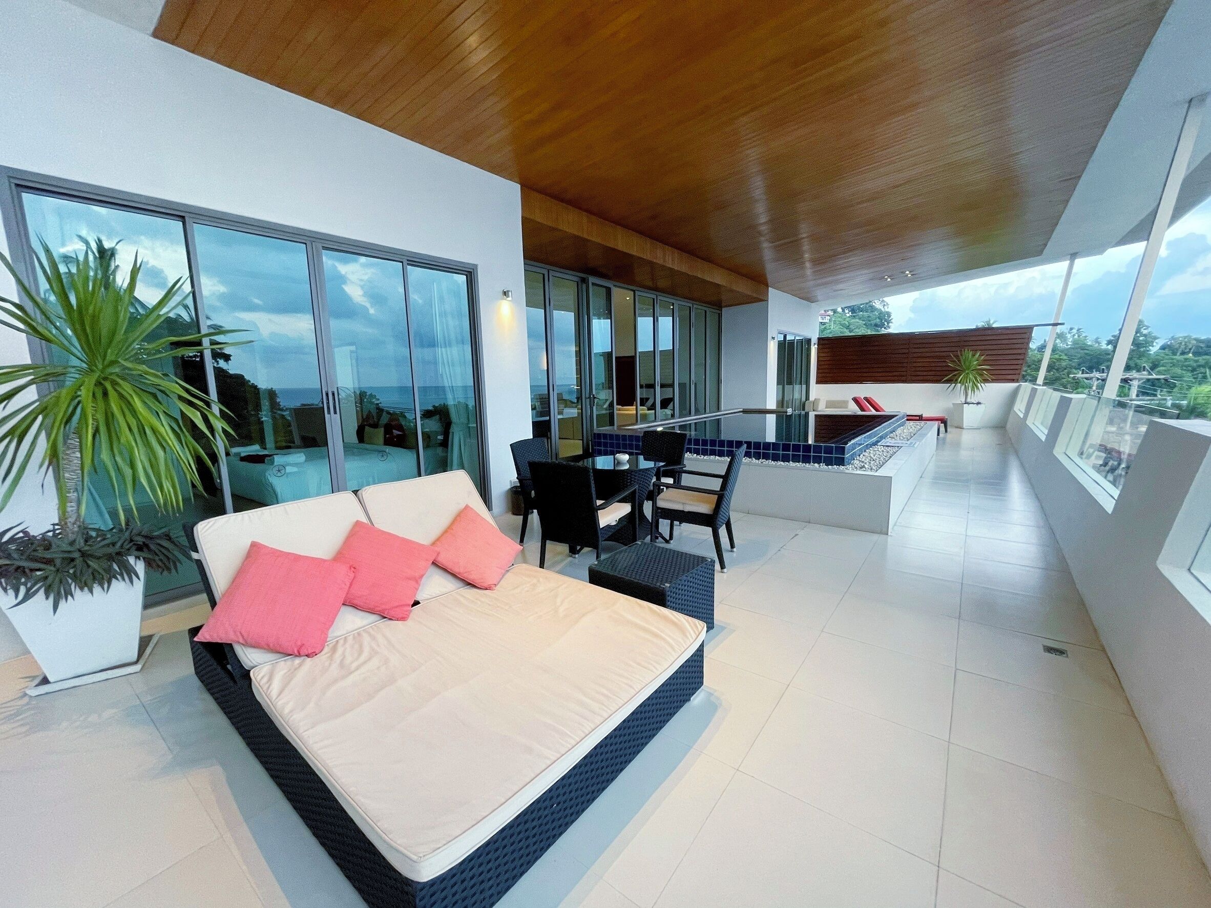 A modern living room with a large sofa, a dining area, and a balcony with a view.