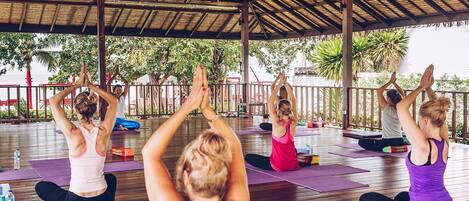 Un grupo de personas practicando yoga en un espacio al aire libre con una terraza de madera y techo de paja.