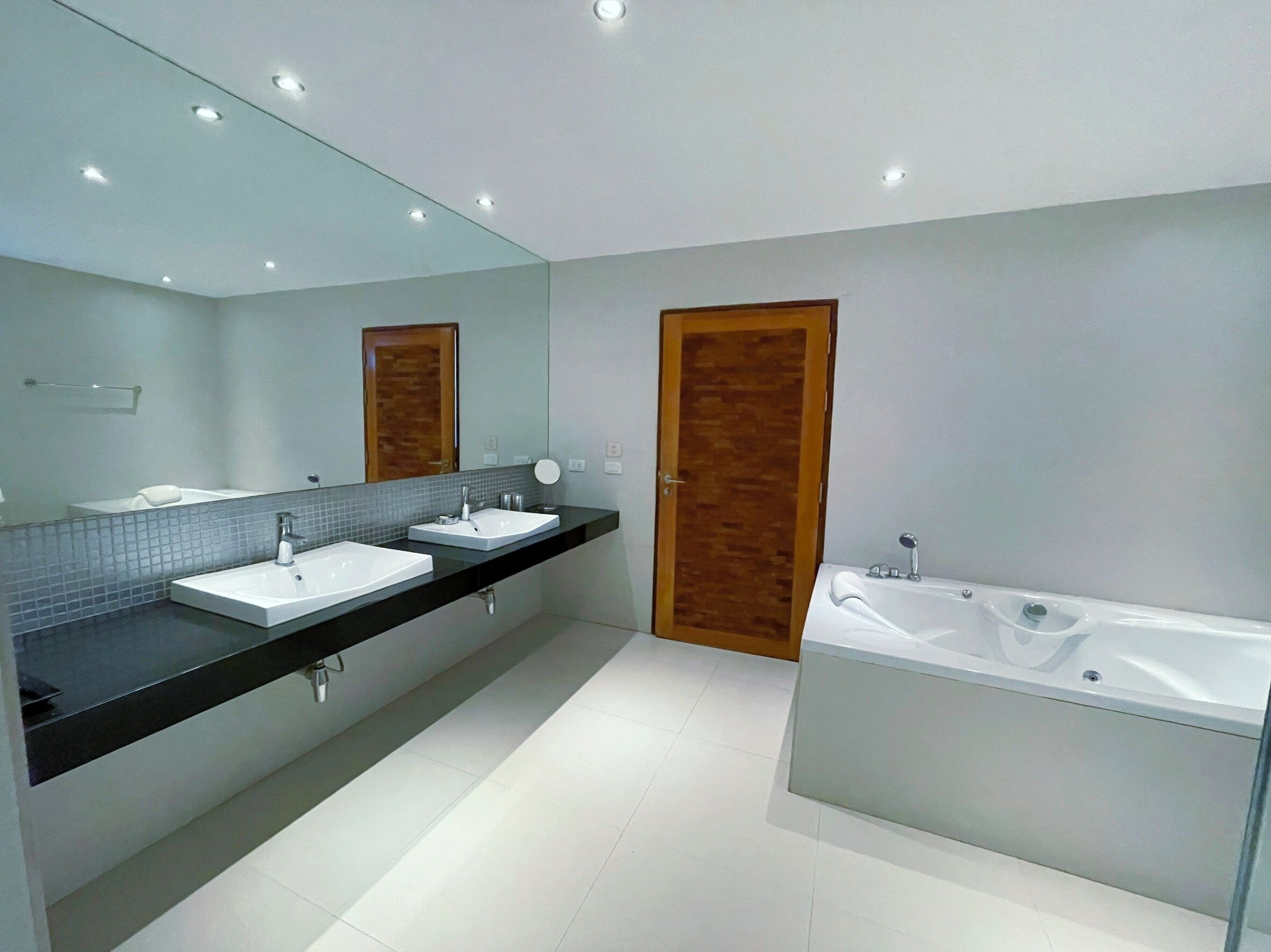 Een moderne badkamer met twee wastafels, een ruim bad en een houten deur.