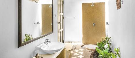 Un baño con un espejo grande, un lavamanos, una ducha y un inodoro pequeño.