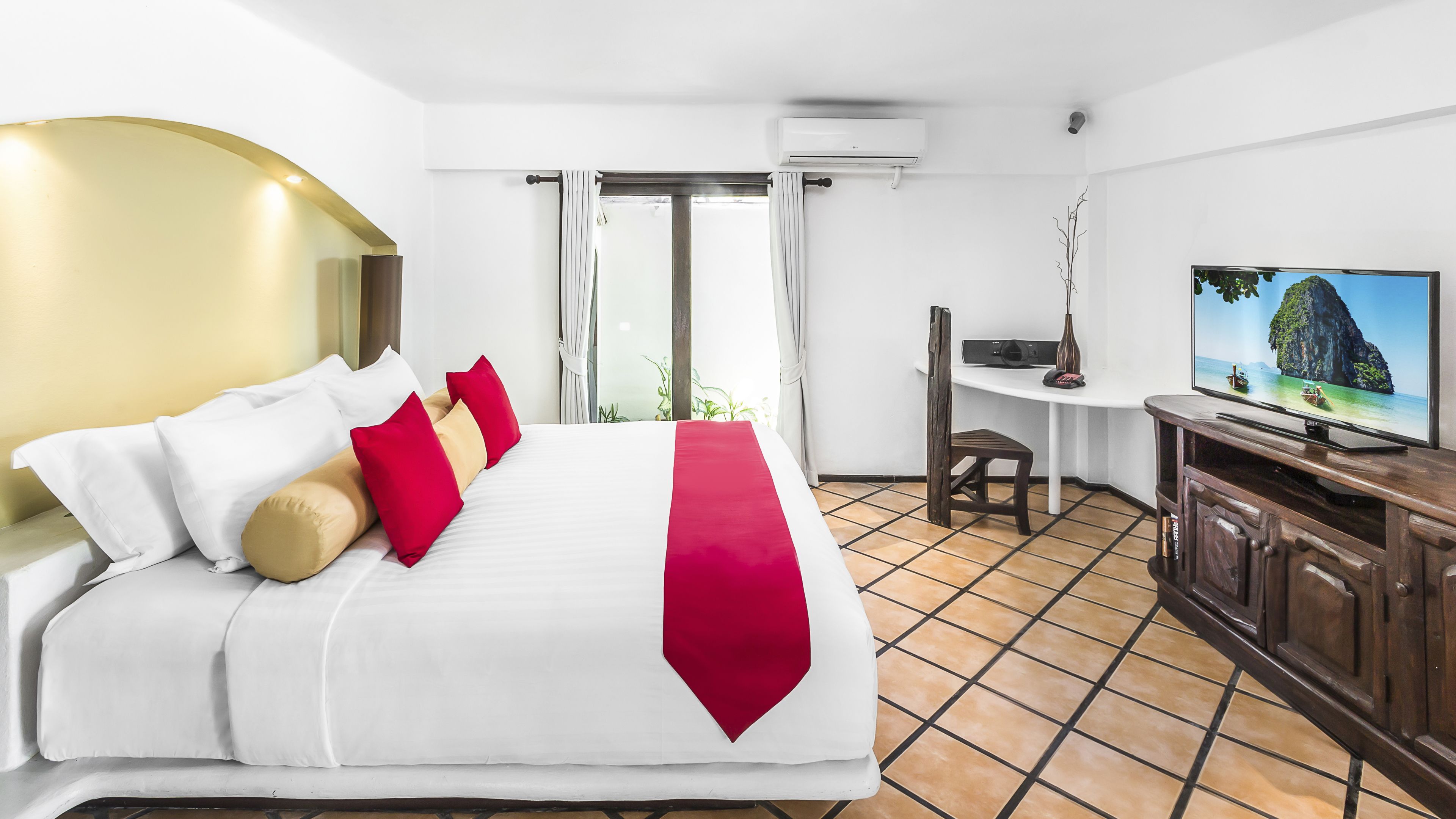 A hotel room with a bed, a desk, a television, and an air conditioning unit.