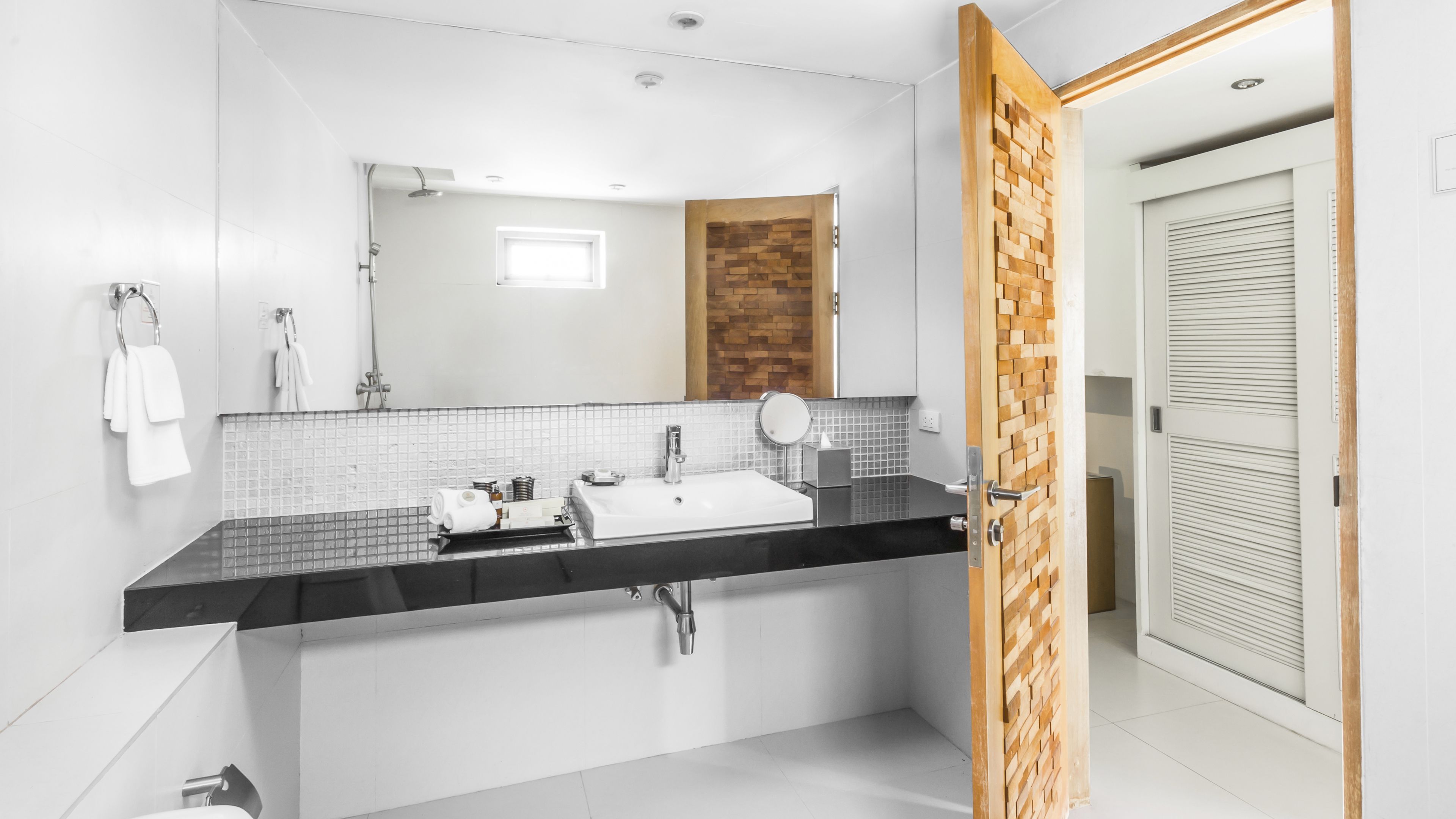 A modern bathroom with a black countertop, white sink, and a wooden accent wall.