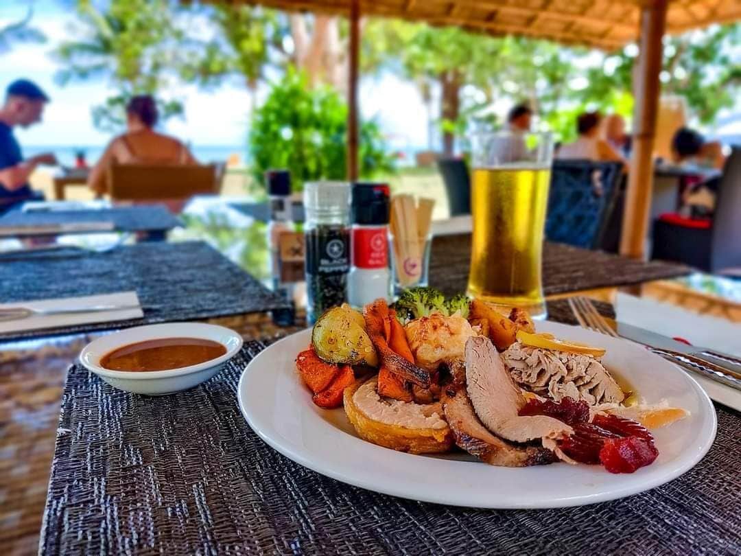 A meal with roasted meats and vegetables on a table, a glass of beer, and condiments.