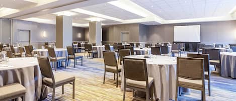 A large conference room with multiple tables and chairs, a projector screen, and a carpeted floor.