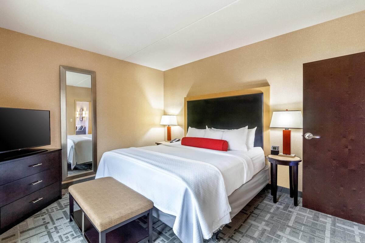 A hotel room with a large bed, a TV, a desk, and a mirror.