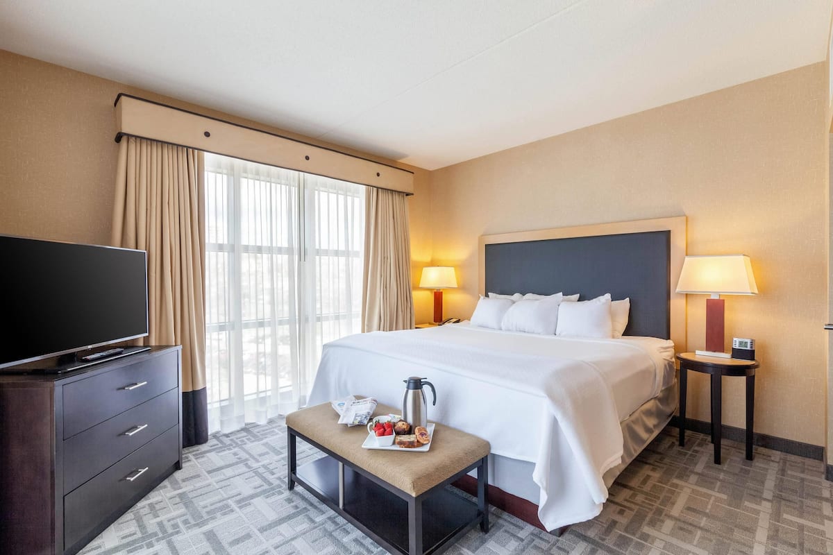A hotel room with a large bed, two bedside lamps, a TV on a dresser, and a small table with breakfast items.