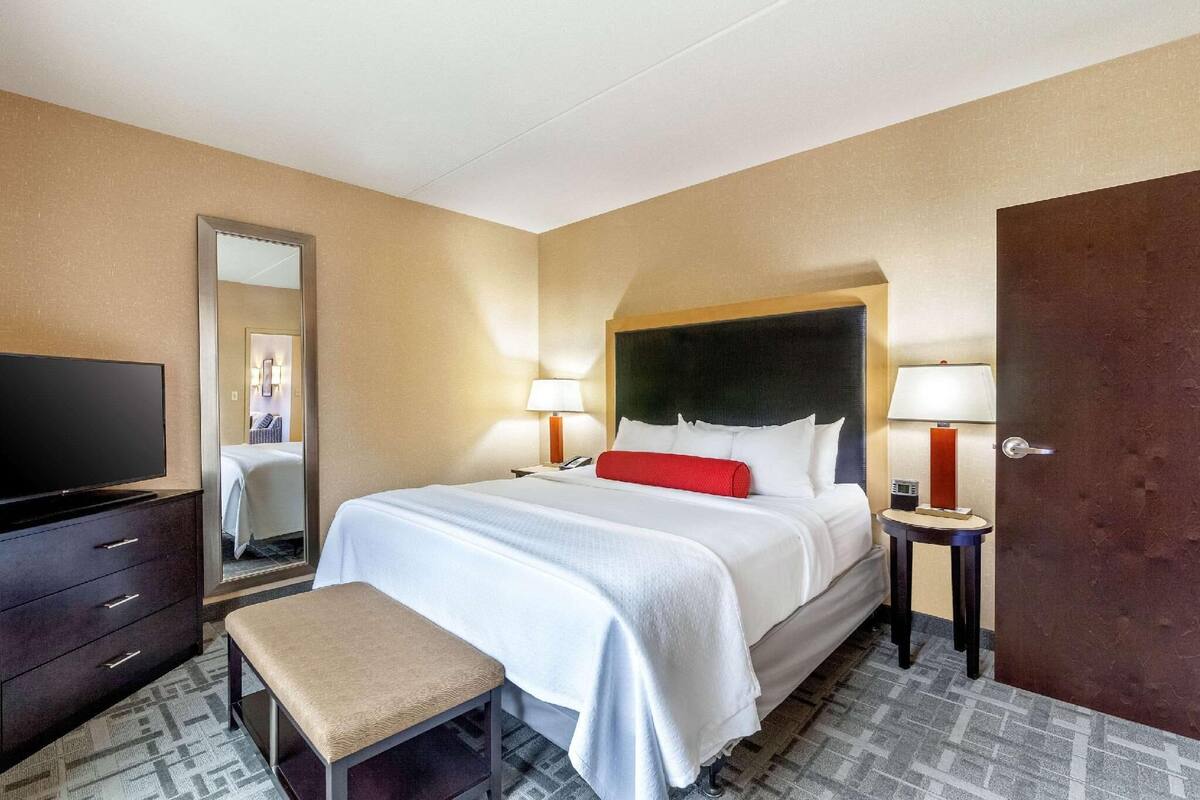 A hotel room with a bed, bedside tables, a TV, a mirror, and a door.
