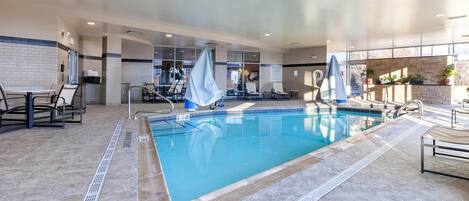 An indoor swimming pool with clear water, surrounded by lounge chairs and a seating area.