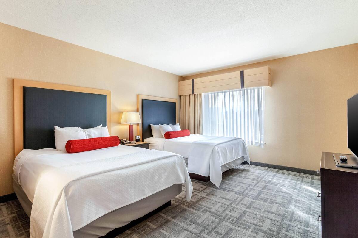 A hotel room with two beds, a desk, a TV, and a window with curtains.