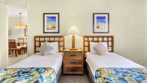 A hotel room with two beds, a nightstand with a lamp, a chair, and framed pictures on the wall. - Hono Koa Vacation Club (Lahaina)