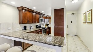 A modern kitchen with granite countertops, stainless steel appliances, and wooden cabinets. - Hono Koa Vacation Club (Lahaina)