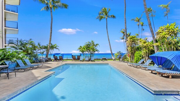 A pool area with lounge chairs and umbrellas, palm trees, and a view of the ocean. - Hono Koa Vacation Club (Lahaina)