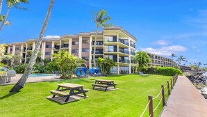 A hotel with multiple balconies, a swimming pool, and a grassy lawn with picnic tables. - Hono Koa Vacation Club (Lahaina)
