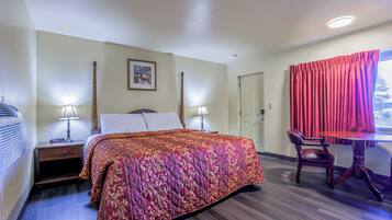 A hotel room with a bed, bedside lamps, a desk with a chair, and a window with curtains.