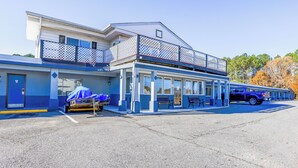 A two-story motel with a covered parking area, a covered outdoor seating area, and a blue and white color scheme. - Whispering Pines by Hotel O Whitestone VA (White Stone)
