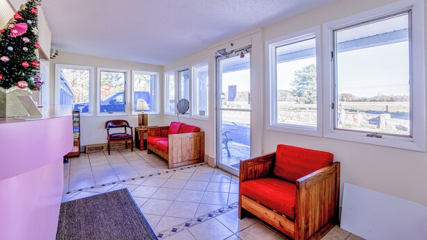 A sunlit room with large windows, a wooden sofa, a red chair, and a Christmas tree. - Whispering Pines by Hotel O Whitestone VA (White Stone)