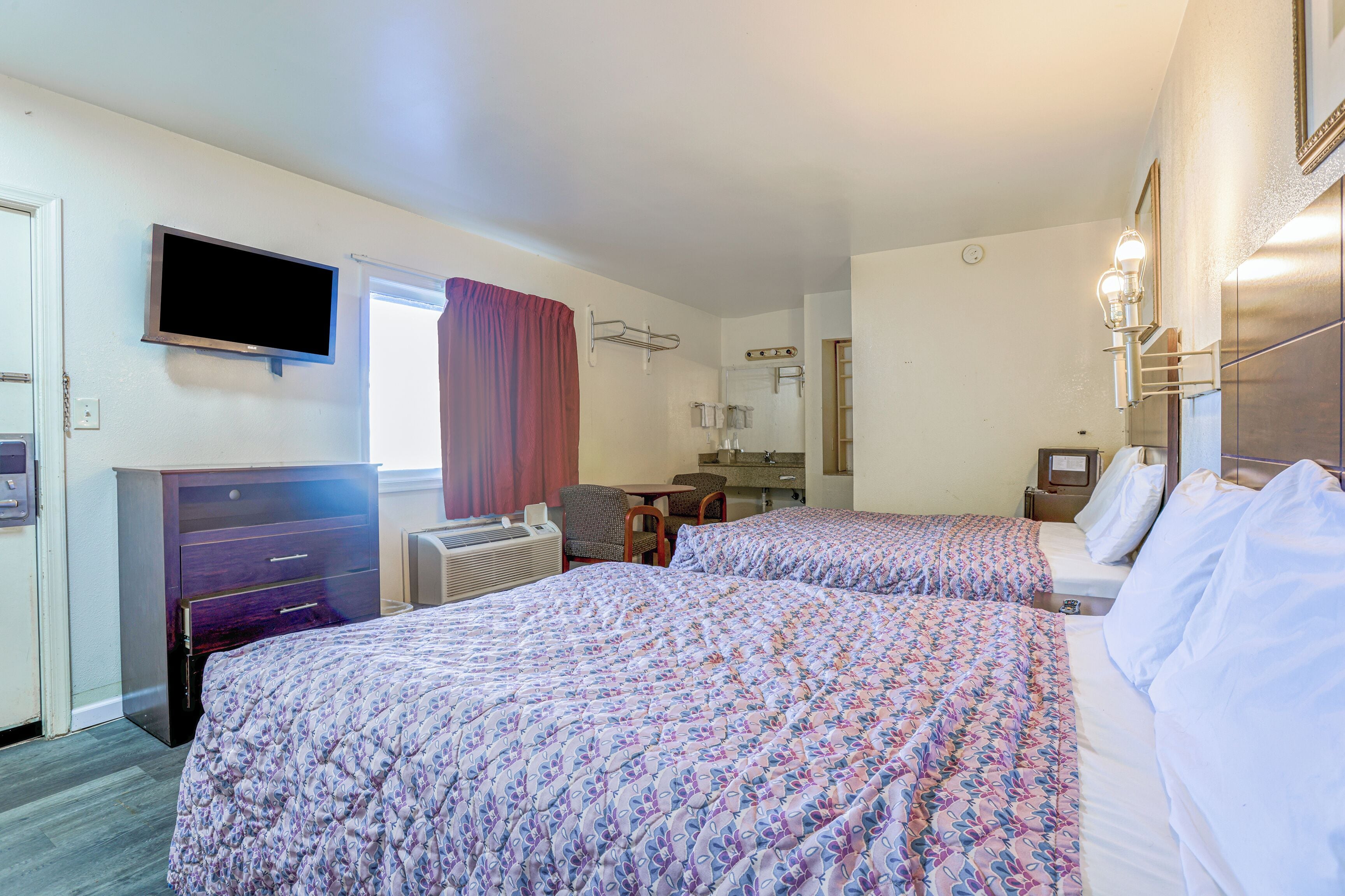 A hotel room with two beds, a TV, a desk, and a chair.