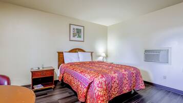 A hotel room with a bed, a nightstand, a table, and a framed picture on the wall.