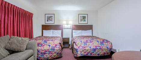 A hotel room with two beds, a sofa, a small table, and two wall-mounted lamps.