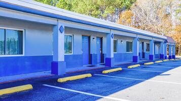 A row of blue and white motel rooms with a parking lot in front.