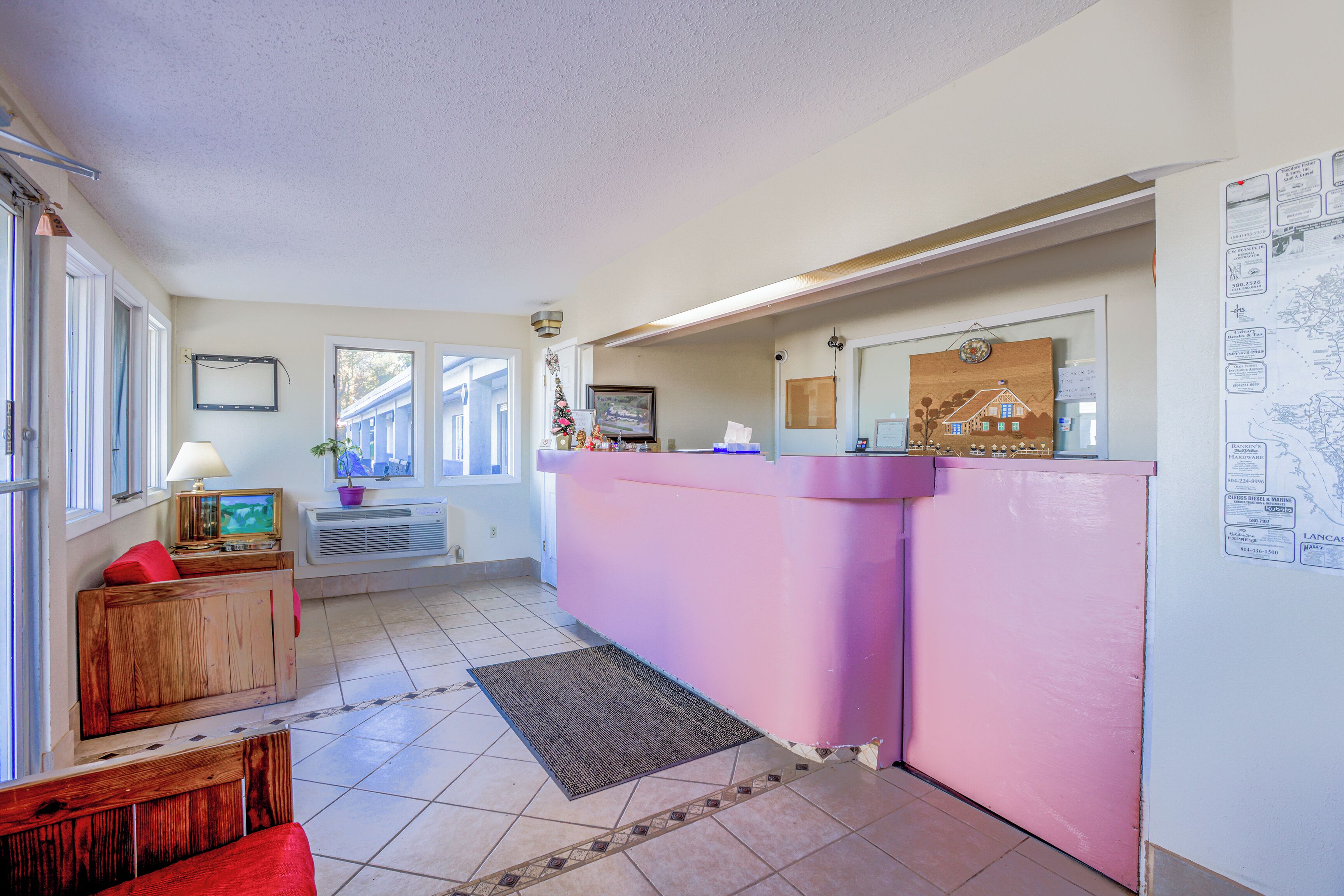 A room with a pink reception desk, a wooden bench, a rug, and a window with blinds.