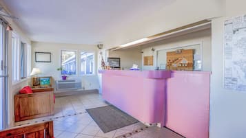 A room with a pink reception desk, a wooden bench, a rug, and a window with blinds.