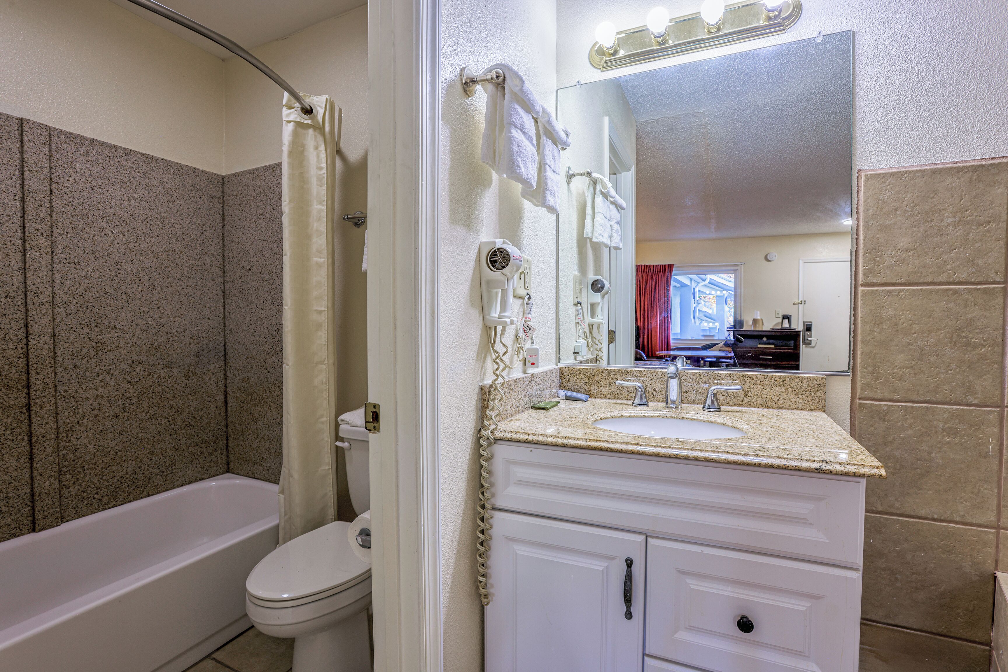 A bathroom with a bathtub, toilet, vanity with a sink, and a mirror.