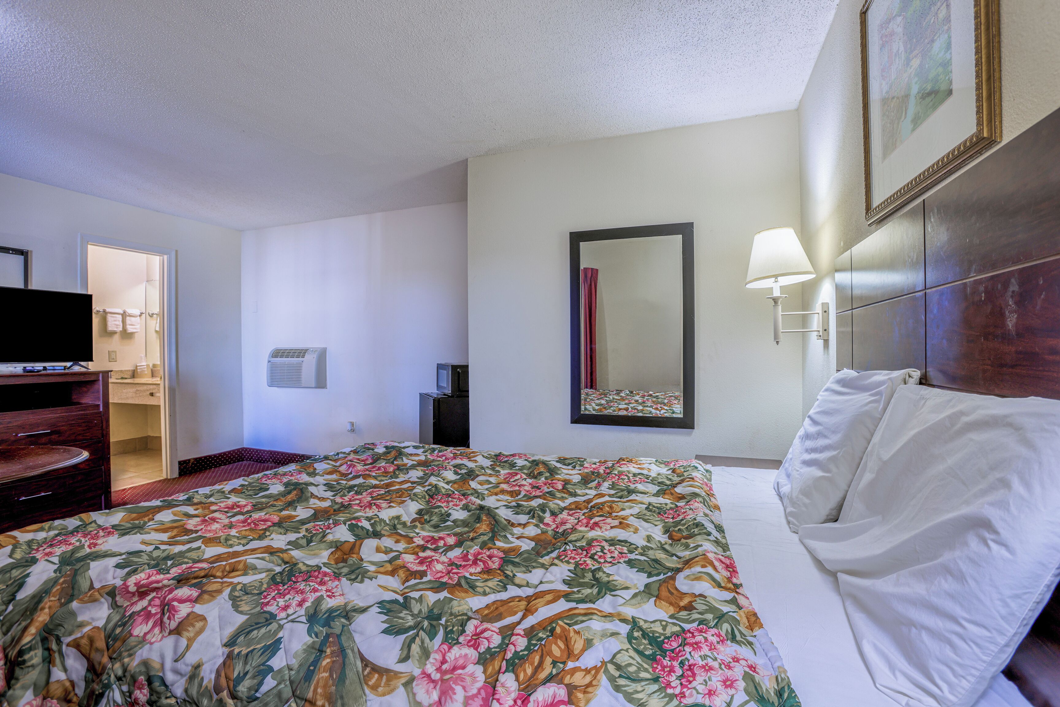 A hotel room with a bed, a television, a dresser, and a door leading to a bathroom.