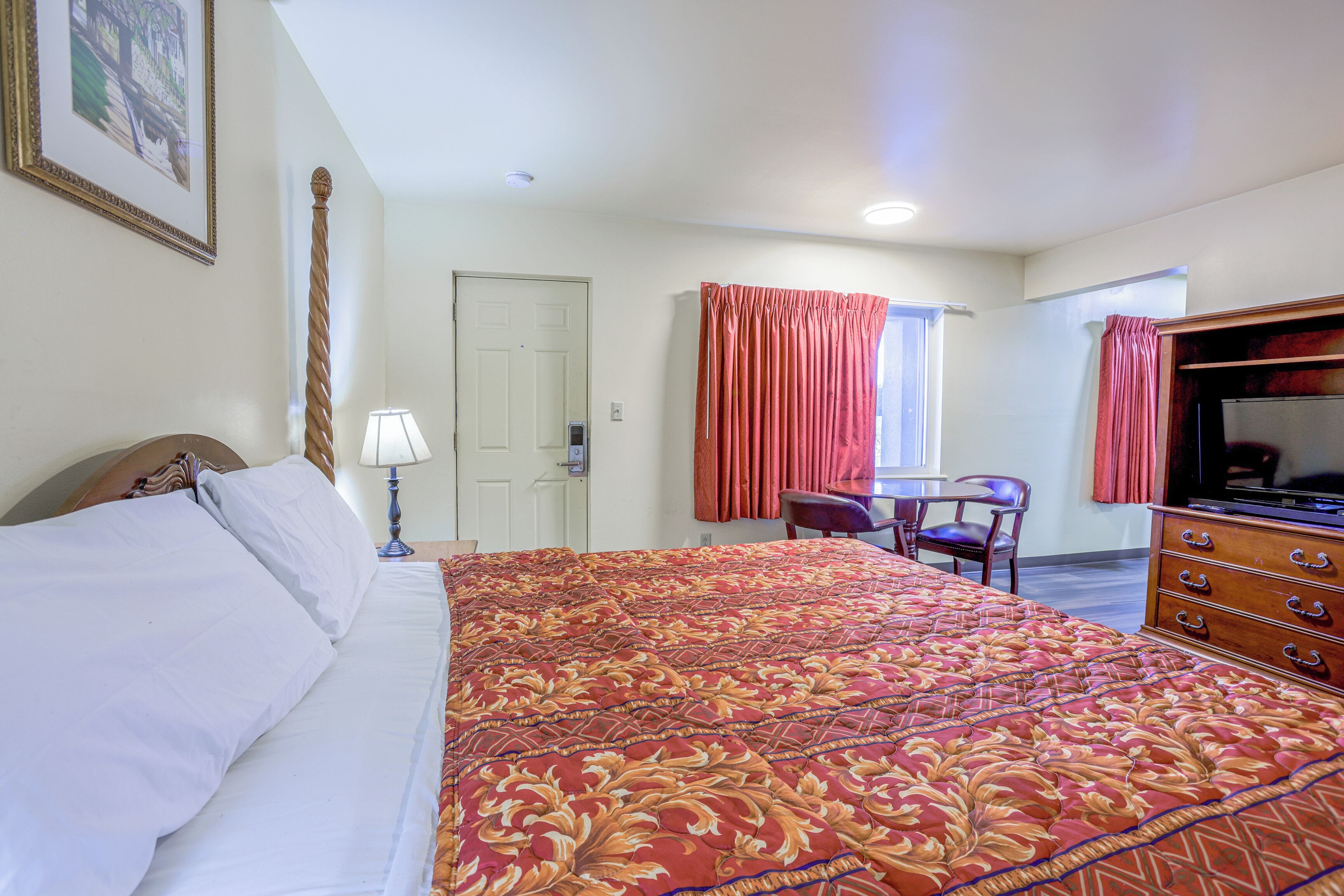 A hotel room with a large bed, a desk, a chair, a television, and a dresser.
