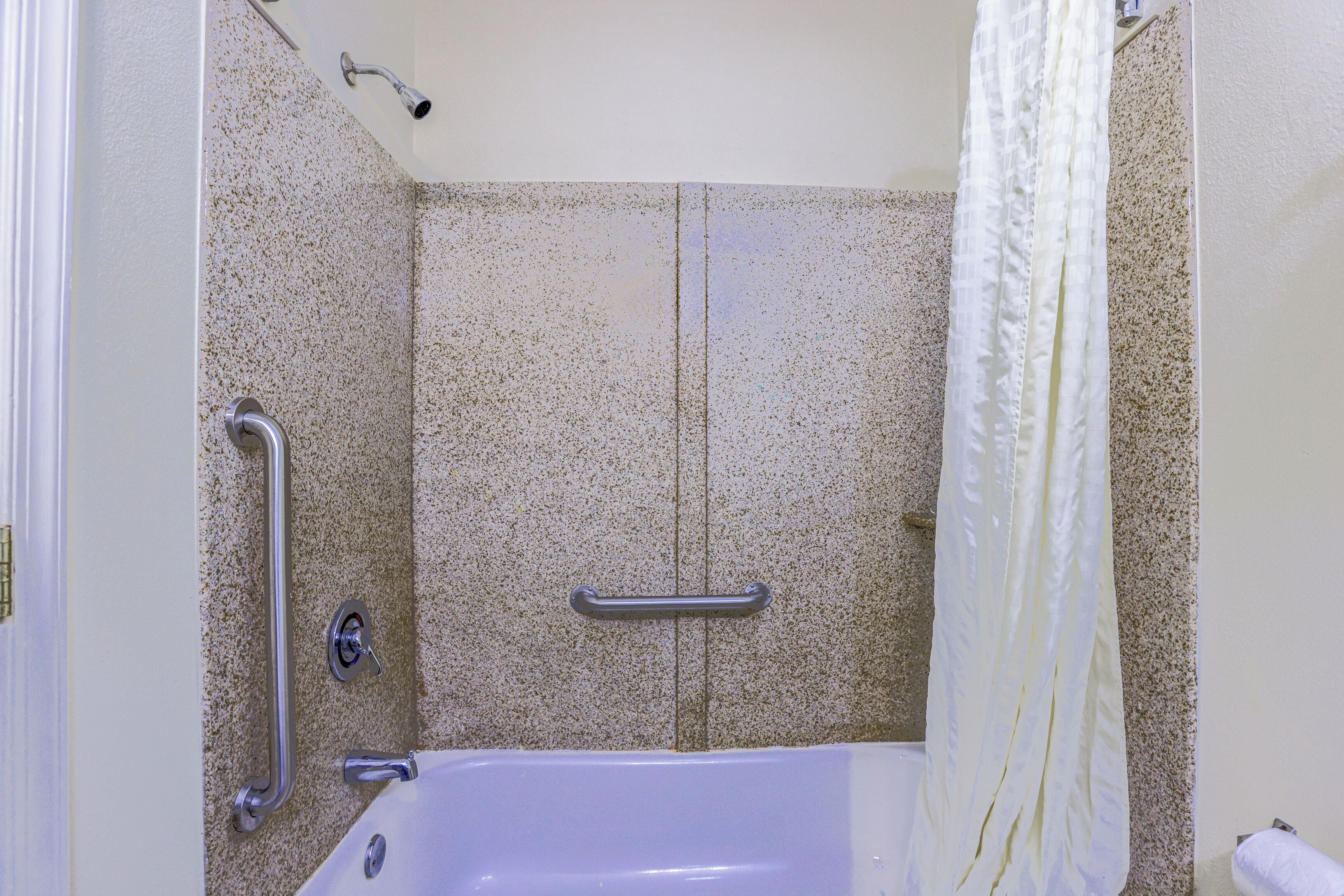 Une salle de bain équipée d’une baignoire, de barres d’appui et d’un rideau de douche.