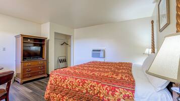 A hotel room with a large bed, a wooden dresser, a television, a wardrobe, and a bedside lamp.