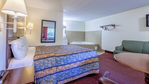 A hotel room with a bed, a sofa, a table, a lamp, a mirror, a window with a view, and a bathroom with a bathtub and sink. - Whispering Pines by Hotel O Whitestone VA (White Stone)