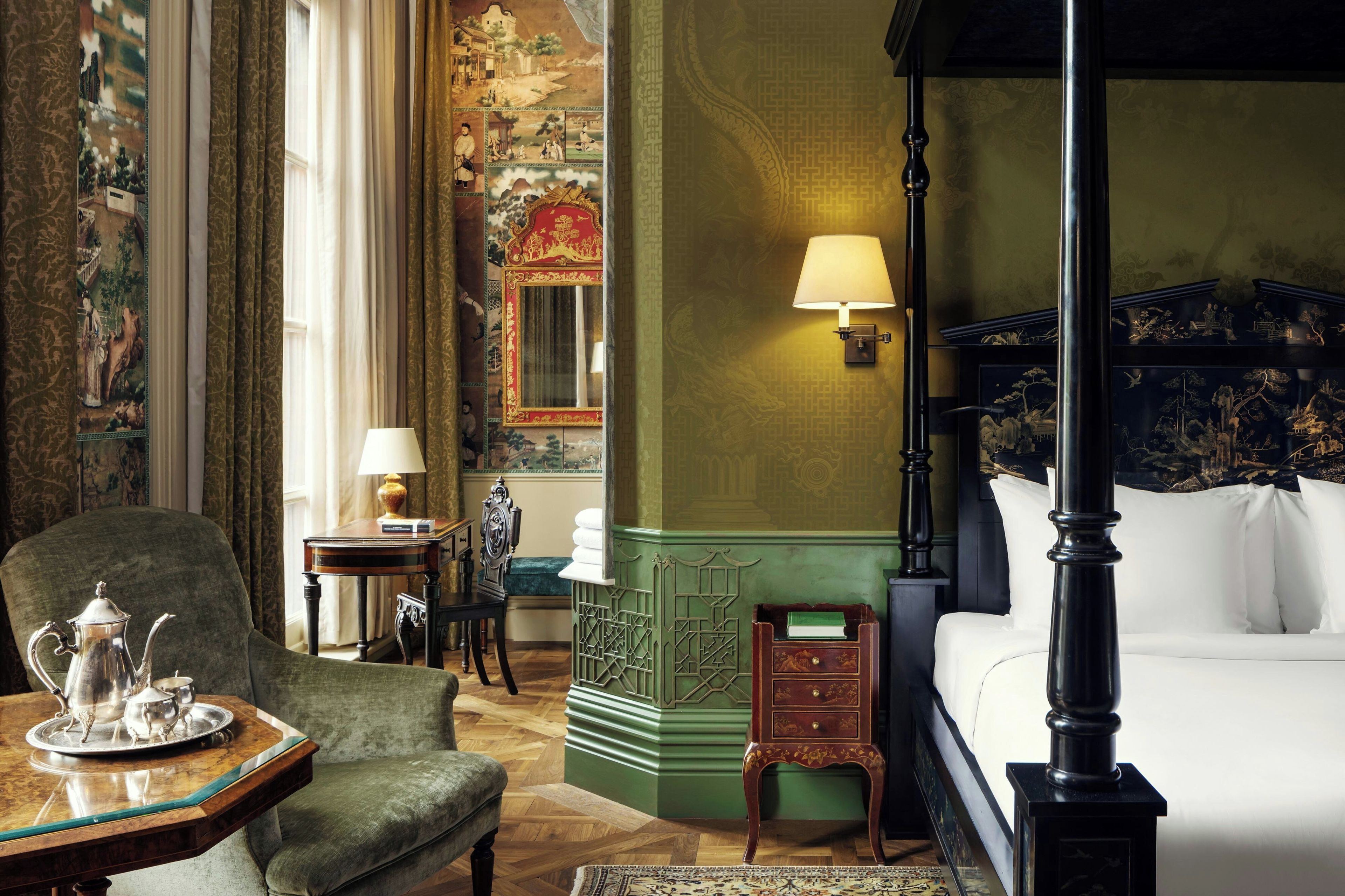 Una habitación tradicional con cama con dosel, una pared de acento verde y un sillón clásico.