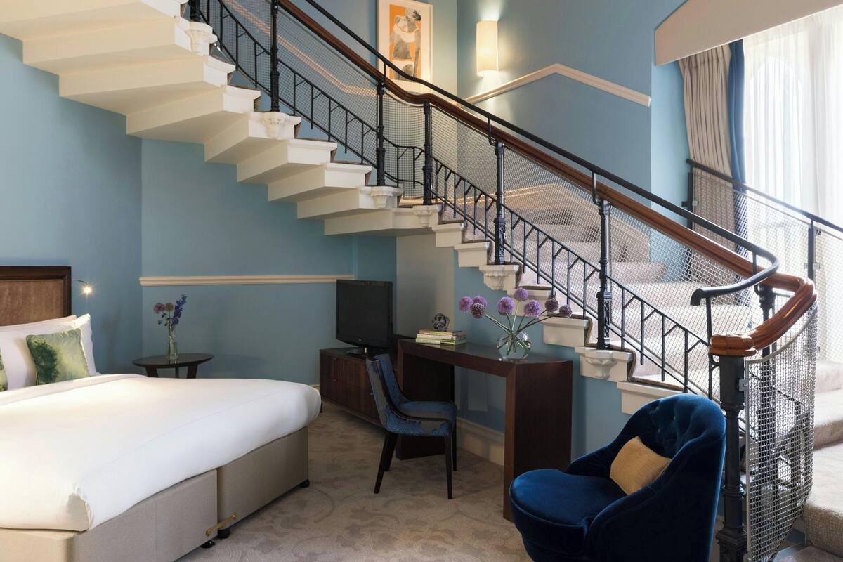 A bedroom with a bed, a desk, a chair, a TV, and a staircase.