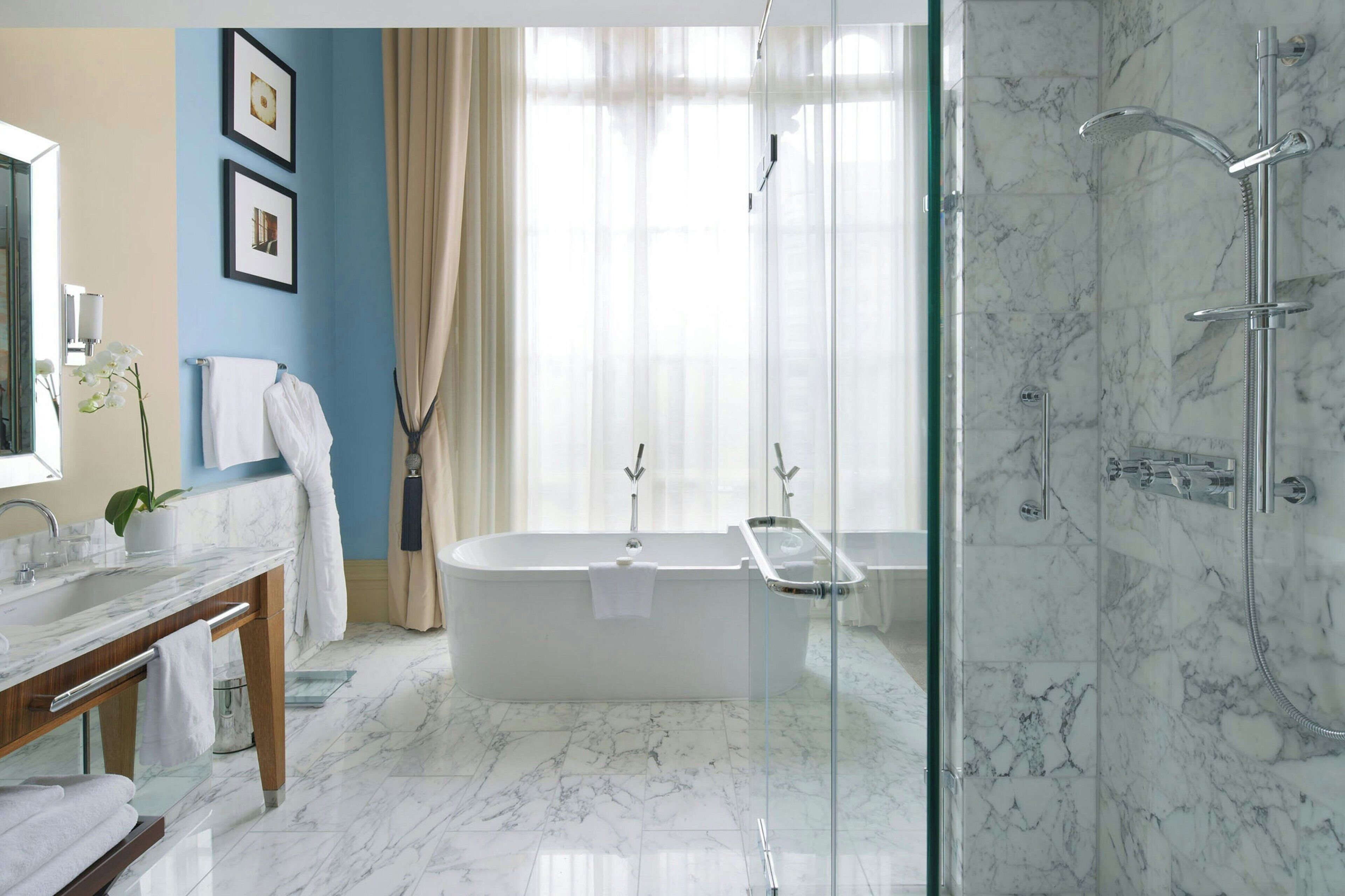 A modern bathroom with a marble floor, a freestanding bathtub, a glass-enclosed shower, and a wooden vanity with a mirror.