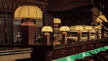 A bar area with multiple stools and lamps, a green patterned wall, and a wooden counter.