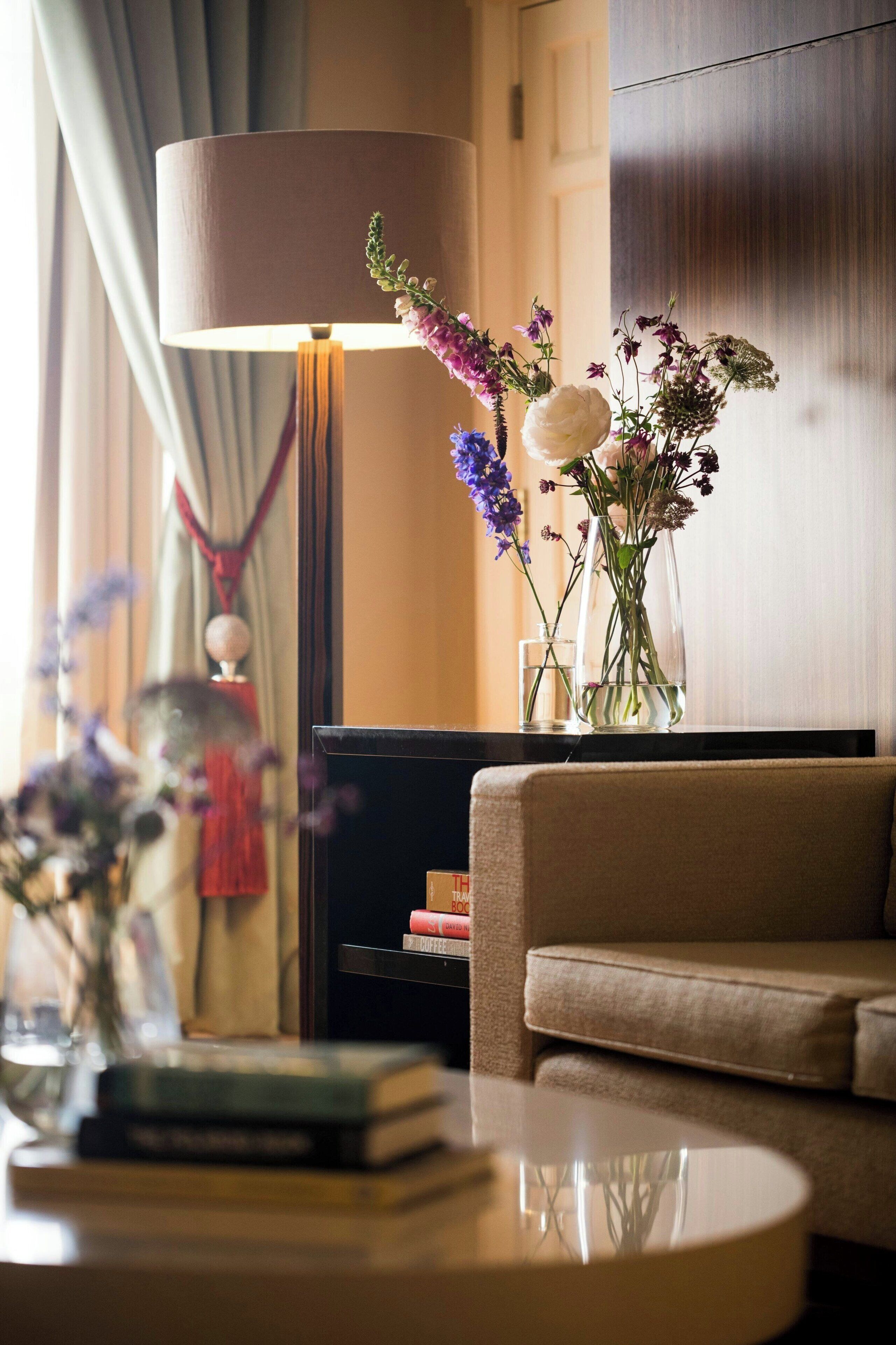 A living room with a sofa, a lamp, and a table with books and a vase of flowers.