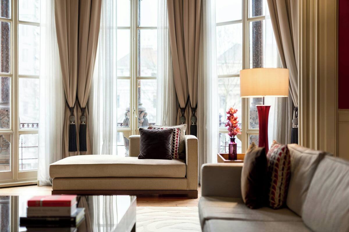 A cozy living room with a sofa, a side table with a lamp, and a window with curtains.