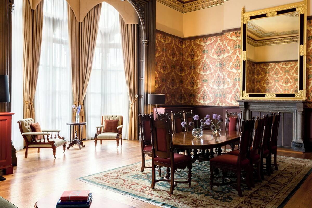 A formal dining room with a wooden table, red upholstered chairs, and a patterned wallpaper.