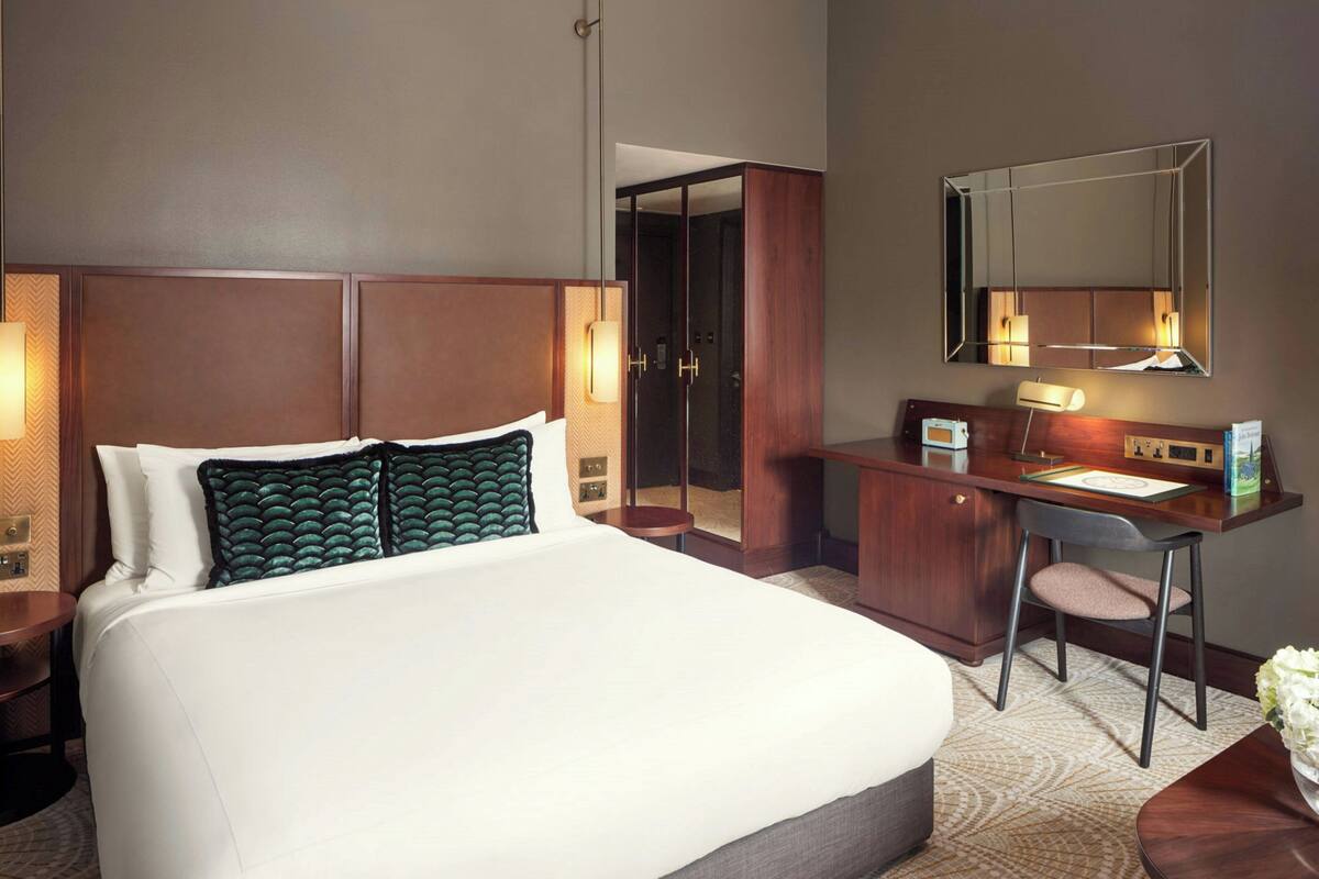 A hotel room with a large bed, a desk, a chair, a mirror, and a walk-in closet.