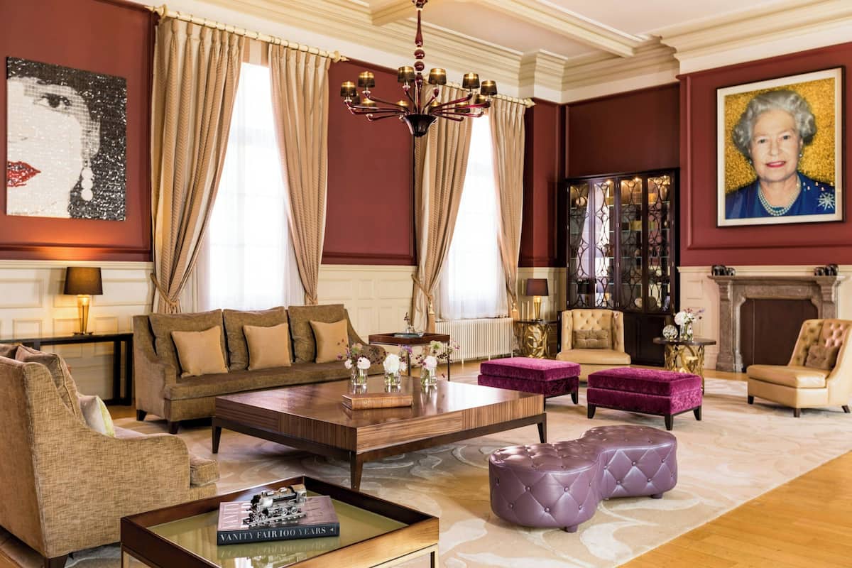 A spacious living room with a large sofa, a coffee table, and a fireplace. There are two armchairs and a purple ottoman.
