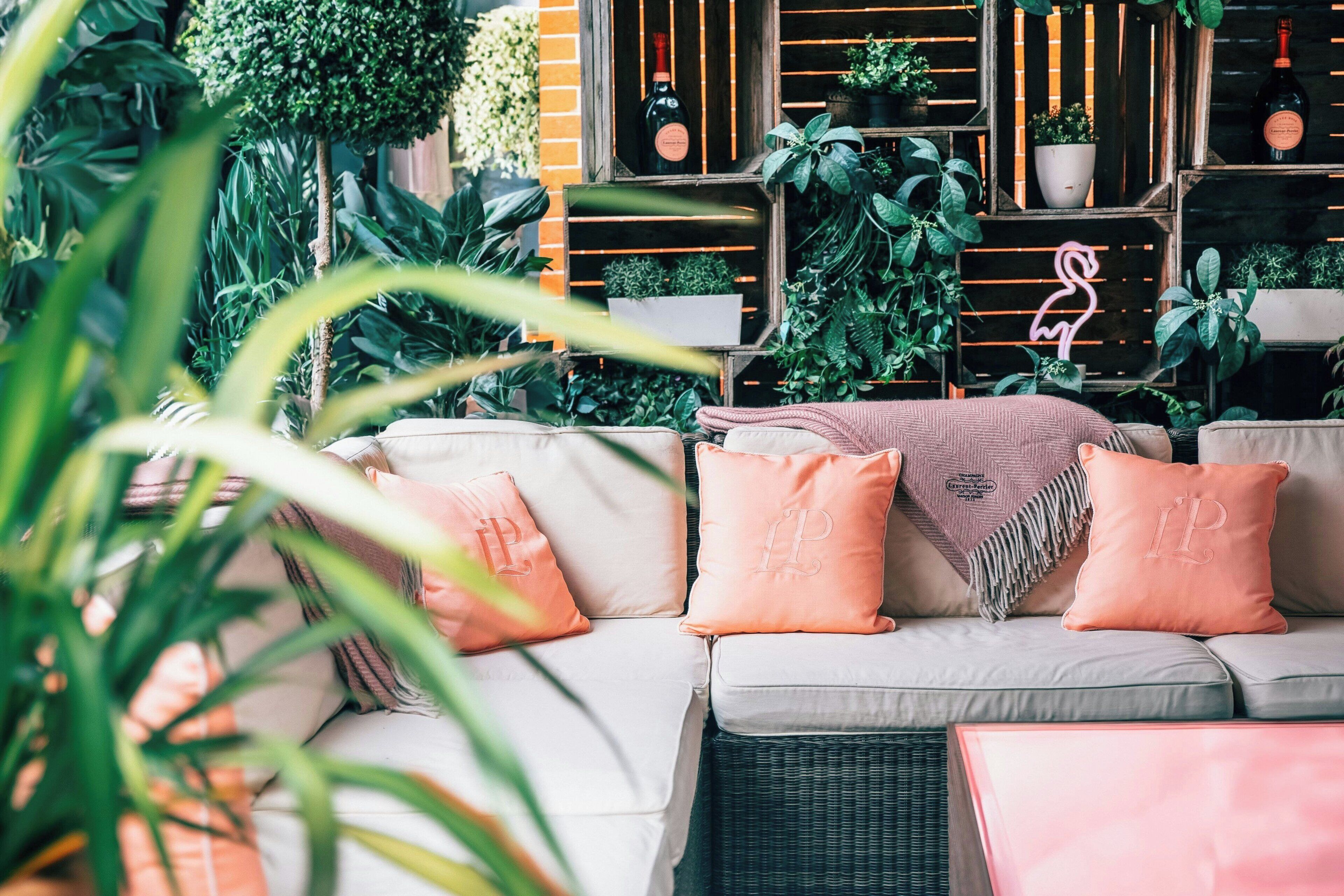 A cozy outdoor seating area with a cushioned sofa, surrounded by lush greenery and potted plants.