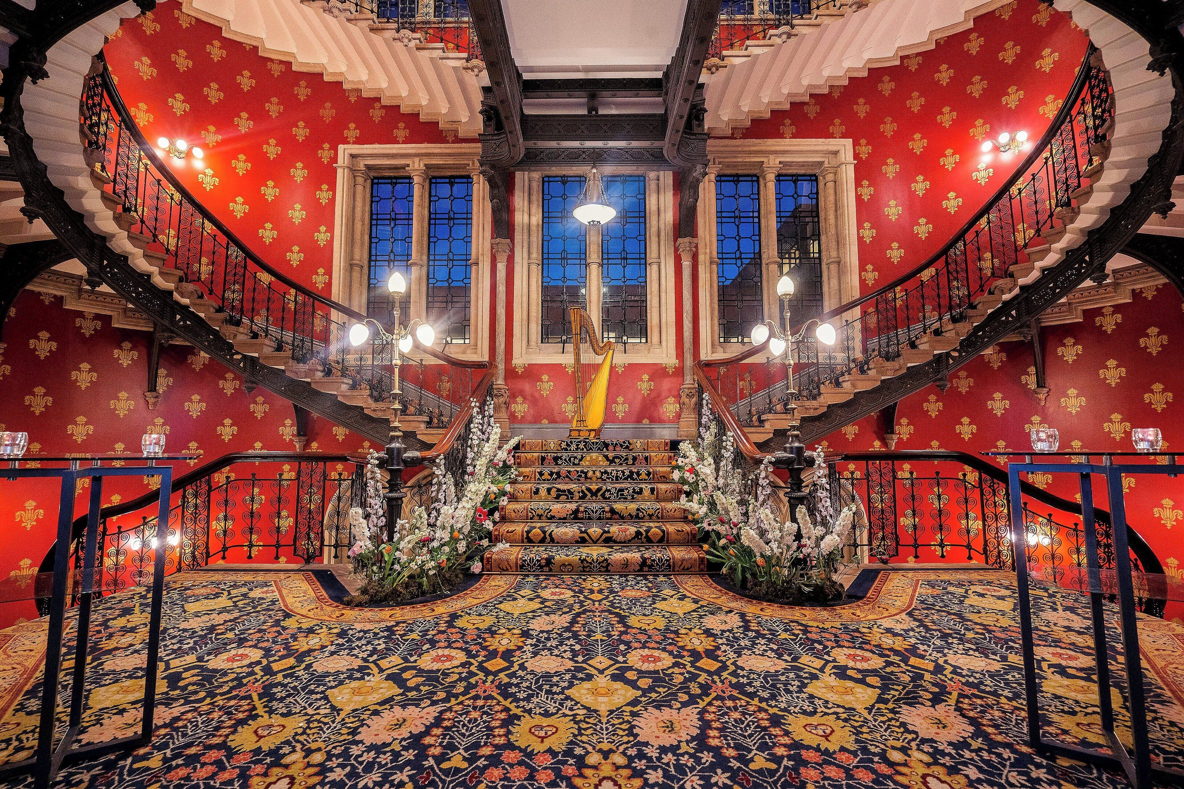 A grand staircase with ornate railings and a patterned carpet leading to a balcony.
