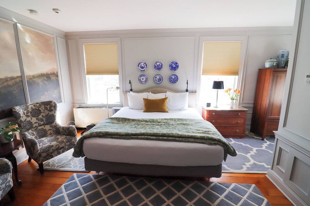 Quarto com uma cama grande, uma cadeira, cômoda e um quadro na parede.