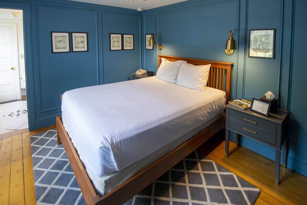 Quarto com cama de madeira, mesa de cabeceira com abajur e quadros nas paredes.